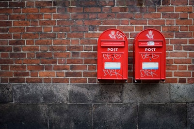 棕色混凝土墙上安装的两个红色邮箱照片